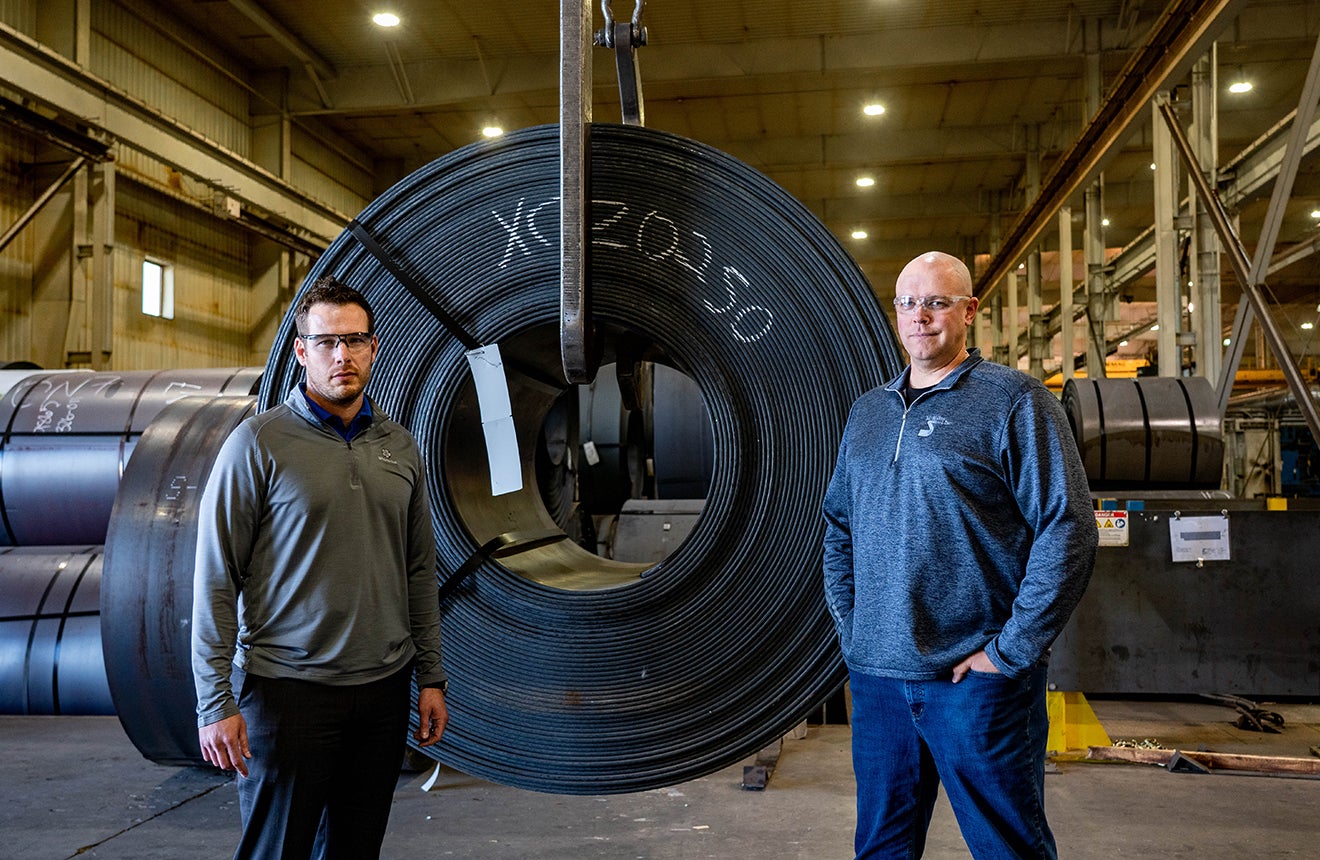 McNeilus Steel general manager Chad Wolf and operations manager Travis Qualley showcase one of the multi-ton coils of steel waiting to be processed at their Fargo facility.