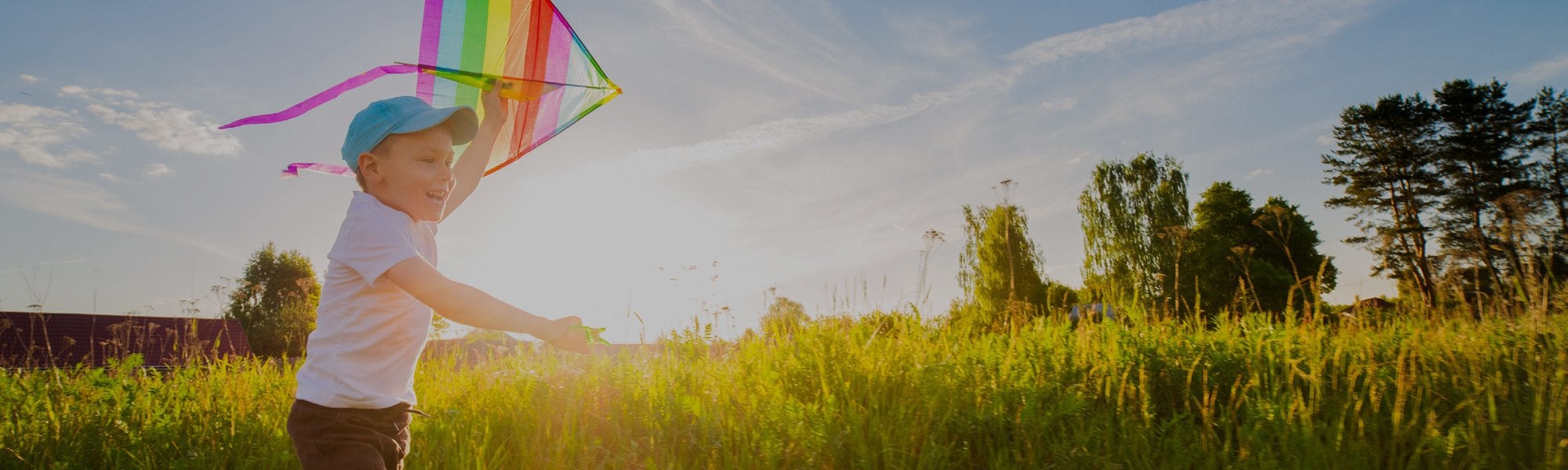 young kid running in a green grassy field with a rainbow kite